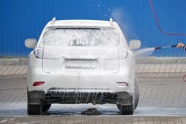 Młody kierowca myjący swój samochód bezdotykowym strumieniem wody pod wysokim ciśnieniem w samoobsługowej myjni samochodowej