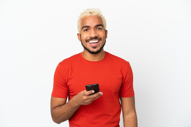 Młody kolumbijski przystojny mężczyzna na białym tle przy użyciu telefonu komórkowego