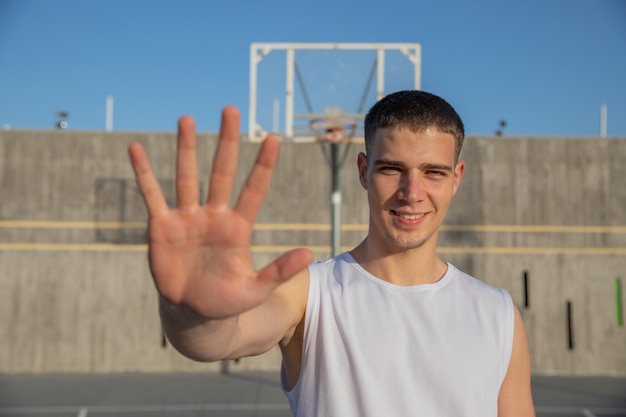 Młody koszykarz na boisku do koszykówki pokazuje dłoń i uśmiecha się