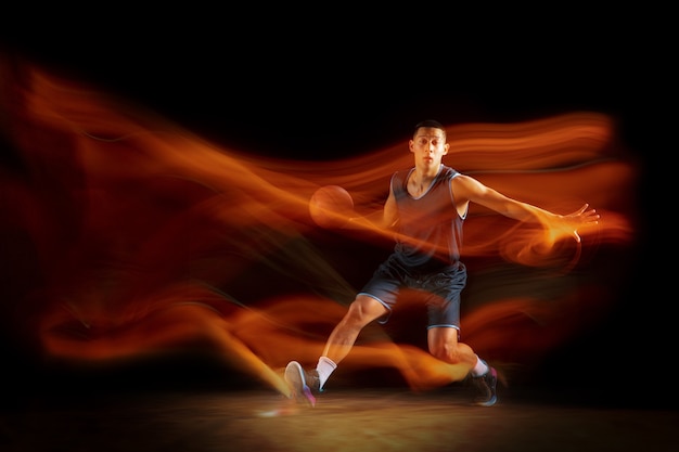 Młody koszykarz z Azji Wschodniej w akcji i skakać w mieszanym świetle na ciemnym tle studio.