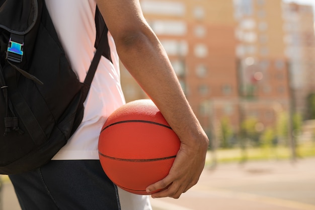 Młody koszykarz z piłką i plecakiem stojący na placu zabaw przed treningiem na świeżym powietrzu