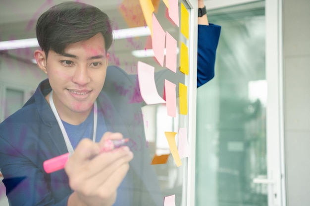 Młody kreatywny biznesmen trzymający marker i piszący plan oraz dzielący się pomysłem na szklanej ścianie