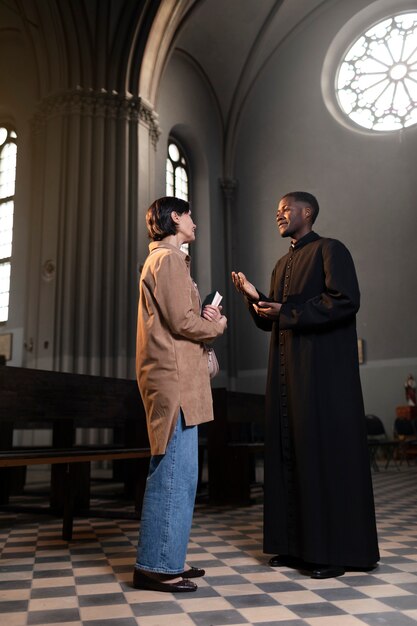 Młody ksiądz i kobieta rozmawiają w kościele, trzymając Biblię