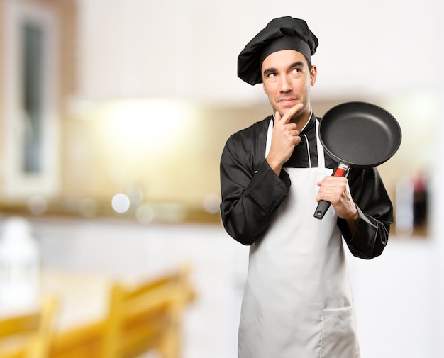 Zdjęcie młody kucharz przy użyciu naczynia do gotowania z gestem wątpliwości