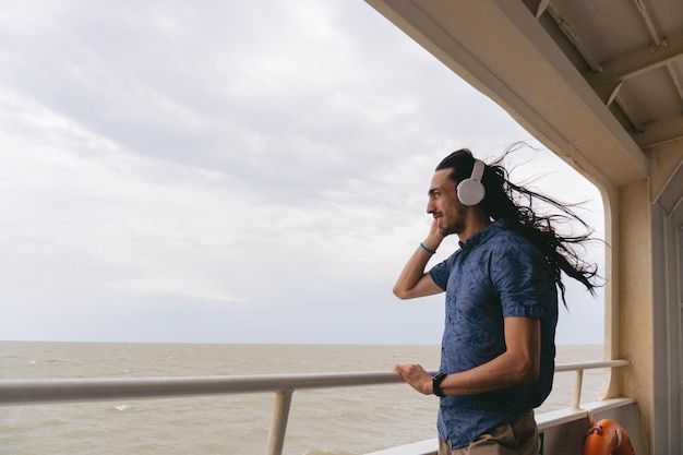 Młody Latynos z długimi włosami słuchający muzyki ze słuchawkami na pokładzie promu Skopiuj miejsce