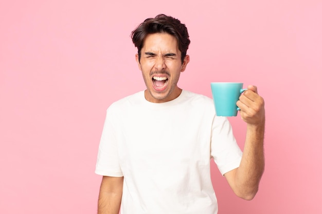 Młody latynoski mężczyzna krzyczy agresywnie, wygląda na bardzo rozgniewanego i trzyma kubek z kawą