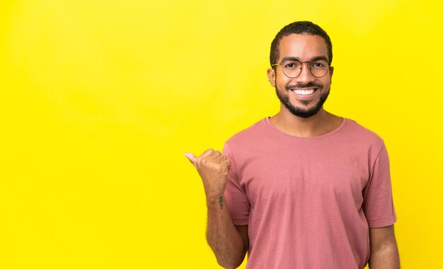 Młody latynoski mężczyzna na żółtym tle wskazujący na bok, aby zaprezentować produkt