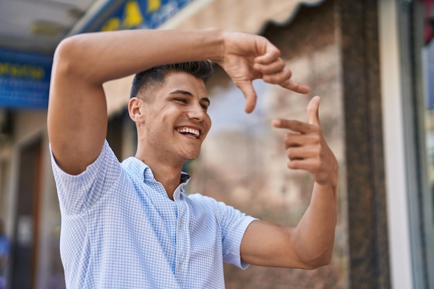 Młody latynoski mężczyzna uśmiecha się pewnie, robiąc gest fotograficzny rękami na ulicy