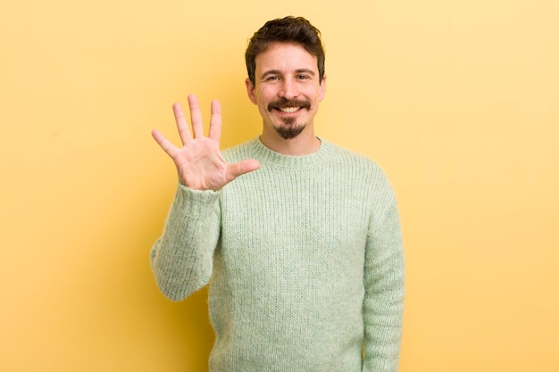 Młody latynoski mężczyzna uśmiechający się i wyglądający przyjaźnie, pokazujący cyfrę piątą lub piątą z ręką do przodu odliczającą