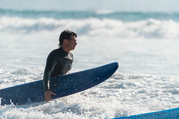 Młody latynoski surfer spacerujący po morzu z deską surfingową w kierunku fal