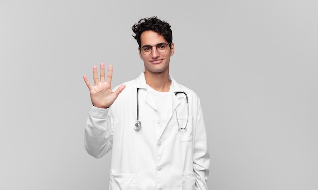 młody lekarz uśmiechnięty i przyjazny wyglądający, pokazujący numer pięć lub piąty z ręką do przodu, odliczający