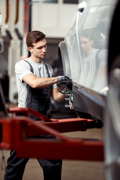 Młody Mechanik Koncentruje Się Na Naprawie Podnoszonego Samochodu.