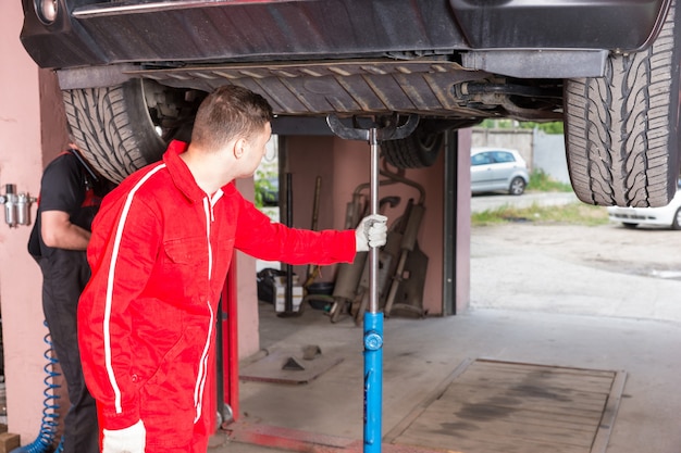 Młody mechanik samochodowy w mundurze trzymającym sprzęt do podnoszenia samochodu