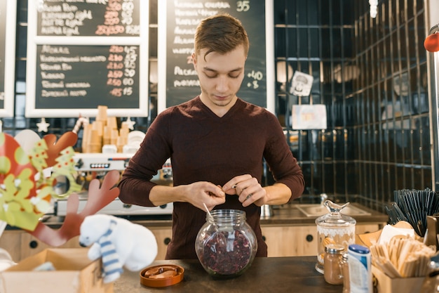 Młody męski barista przygotowywa czerwoną naturalną ziołową herbatę