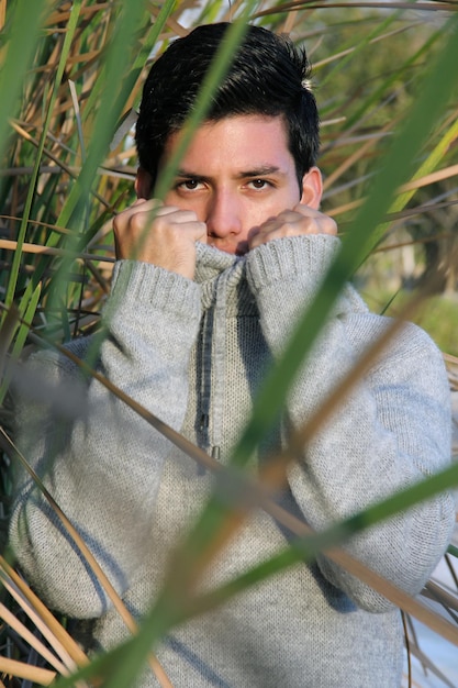 młody męski model w szarym swetrze wśród trawy