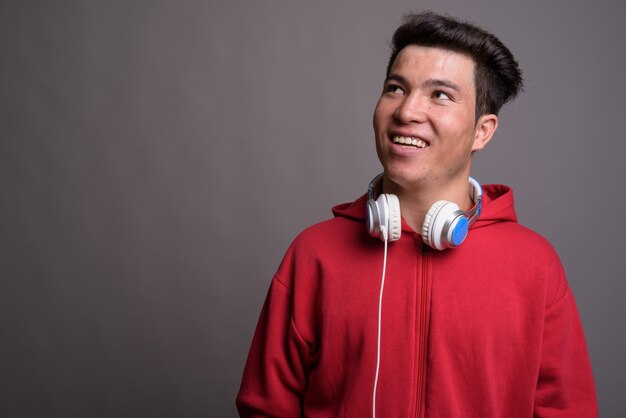 Młody mężczyzna Azji noszenie słuchawek przed szarej ścianie
