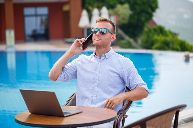 Młody mężczyzna biznesmen z laptopem obsiadaniem przy basenie. Otwarte miejsce pracy. Koncepcja freelancera. Zakupy online. Praca wakacyjna