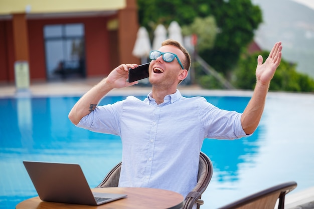 Młody mężczyzna biznesmen z laptopem obsiadaniem przy basenie. Otwarte miejsce pracy. Koncepcja freelancera. Zakupy online. Praca wakacyjna