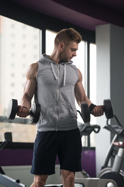 Młody mężczyzna ćwiczący bicepsy w lokach z hantlami na siłowni