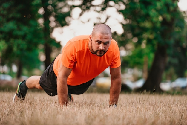 Młody mężczyzna ćwiczący robienie pompek w parku, gdy rozgrzewa się do codziennego treningu lub joggingu