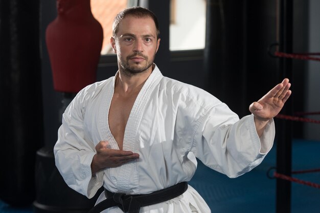 Młody mężczyzna ćwiczący swoje karate porusza białe kimono w czarnym pasie