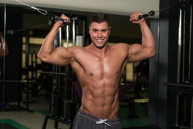 Młody mężczyzna ćwiczy na bicepsie ze skrzyżowaniem kabli w nowoczesnej siłowni