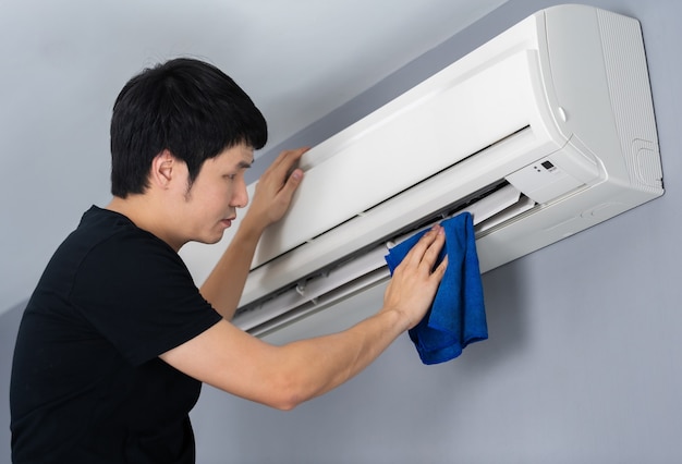 Młody mężczyzna czyści klimatyzator szmatką w domu