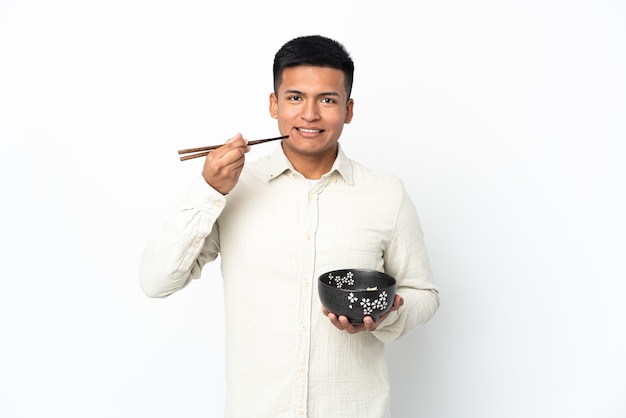 Młody mężczyzna Ekwadoru na białej ścianie trzyma miskę makaronu pałeczkami
