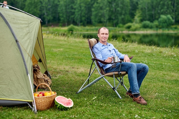 Młody Mężczyzna Freelancer Siedzi Na Krześle I Relaksuje Się Przed Namiotem Na Kempingu W Lesie Lub Na łące Aktywność Na świeżym Powietrzu Latem Przygoda Podróżowanie W Parku Narodowym Wypoczynek Wakacje Relaks