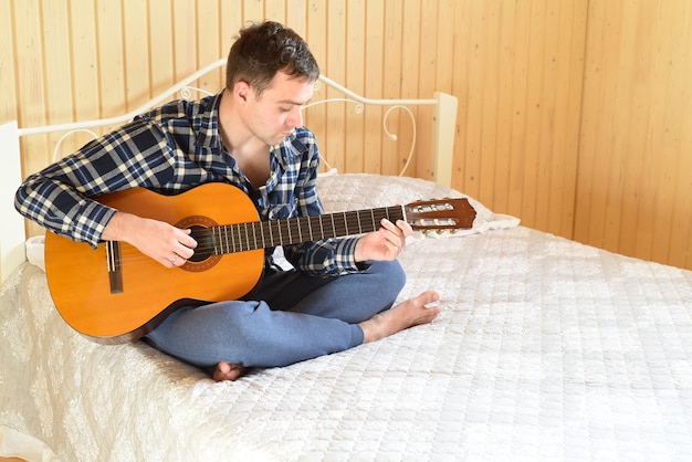 Młody mężczyzna gra na gitarze i siedzi na łóżku