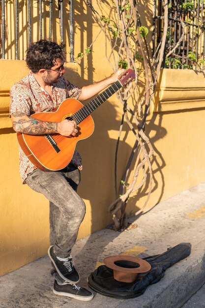 Młody mężczyzna gra na gitarze stojąc na ulicy