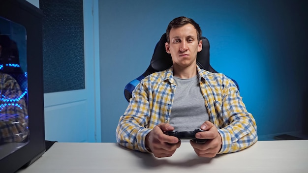 Zdjęcie młody mężczyzna gra w grę komputerową z gamepadem w półciemnym pokoju