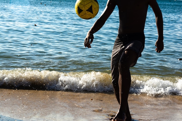 Zdjęcie młody mężczyzna gra w piłkę nożną na plaży riberia w mieście salvador bahia