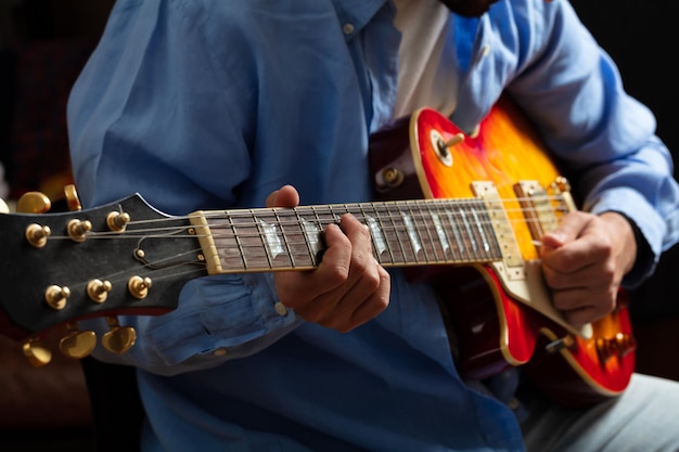 Młody mężczyzna grający na gitarze z bliska widok ciemnego tła