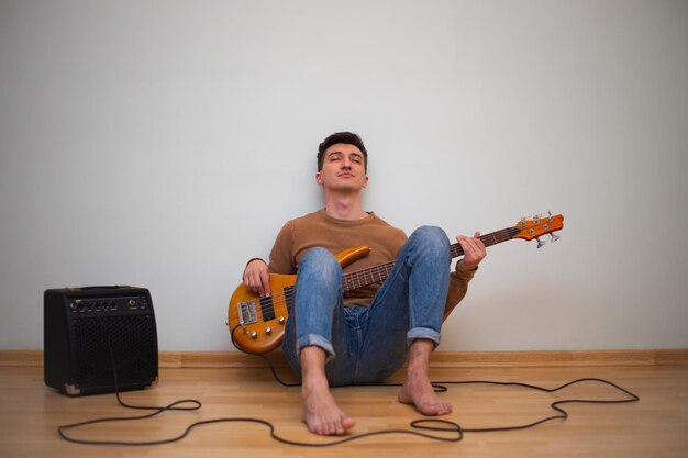 Młody mężczyzna grający na gitarze ze ścianą w tle