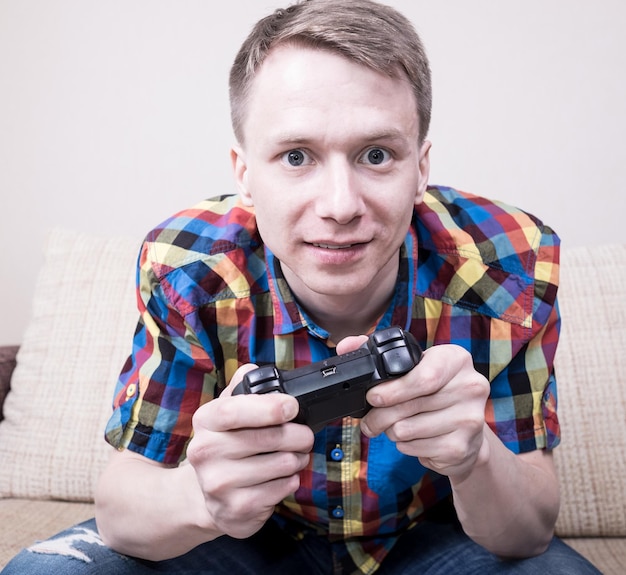 Zdjęcie młody mężczyzna grający w gry wideo, siedzący na sofie i trzymający pilota