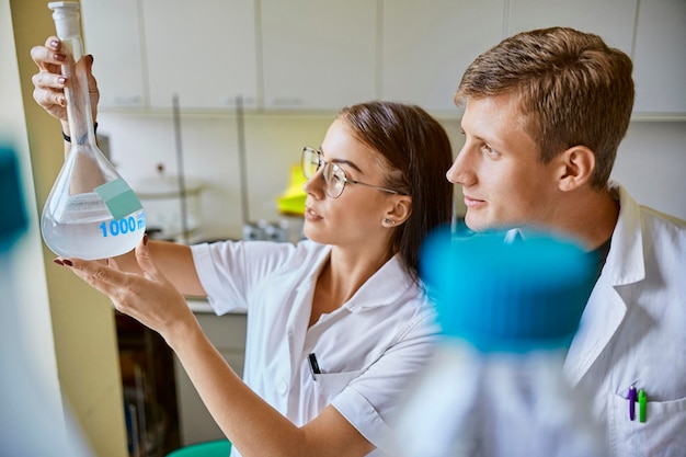 Zdjęcie młody mężczyzna i kobieta patrząc na płyn w kolbie w laboratorium