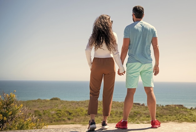 Młody mężczyzna i kobieta trzymający się za ręce, patrzący na morze z góry widok z tyłu, miłość