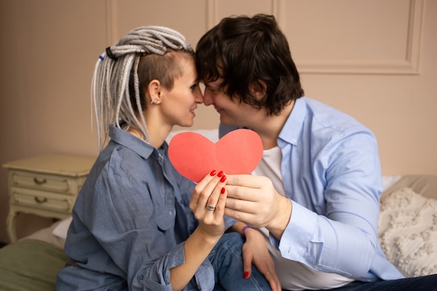 Młody mężczyzna i kobieta w domu całuje z czerwonym sercem valentine w rękach.