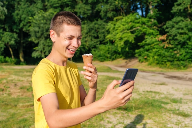 Młody mężczyzna je lody i używa smartfona na zewnątrz