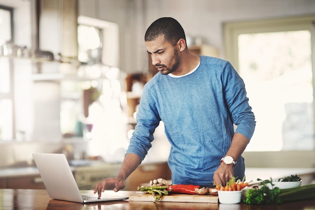 Młody Mężczyzna Korzystający Z Laptopa Podczas Gotowania W Kuchni, Sprawdzający Internet Mężczyzna Ogląda Samouczek Online Podczas Przygotowywania Zdrowego, Ekologicznego Domowego Posiłku Facet Przestrzegający Prostego Wegetariańskiego Przepisu