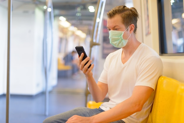 Młody mężczyzna korzystający z telefonu w pociągu z maską do ochrony przed epidemią wirusa koronowego