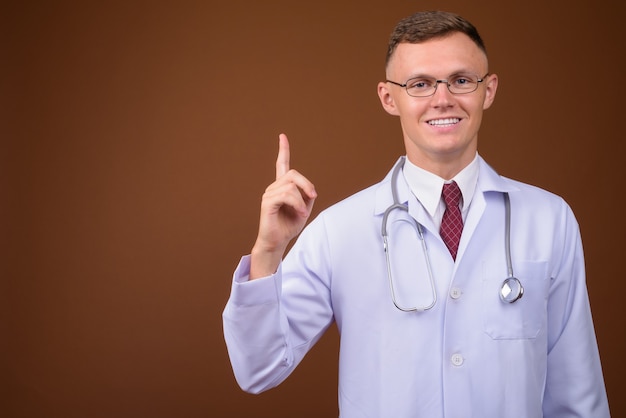 Młody mężczyzna lekarz noszenie okularów na brązowym tle