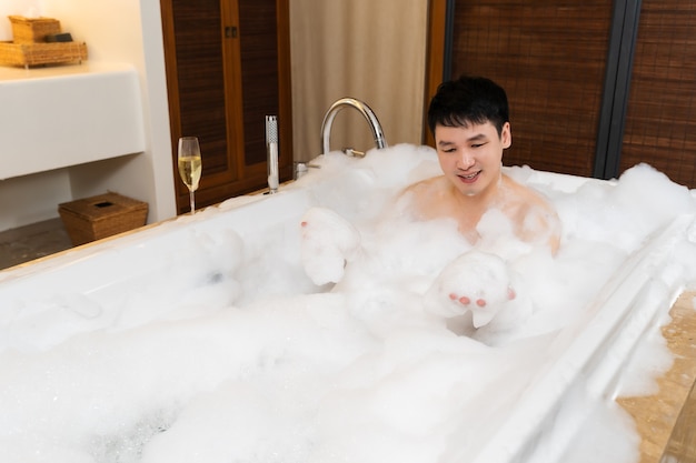 Młody mężczyzna myje ciało i bawi się pianką bąbelkową w wannie