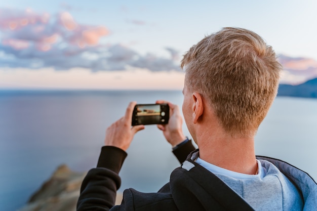 Młody Mężczyzna Na Szczycie Góry Robi Zdjęcie Smartfonem Z Oszałamiającym Widokiem Na Zachód Słońca