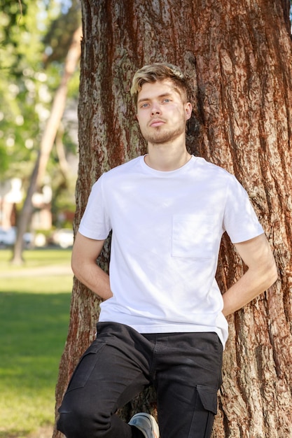 Młody mężczyzna oparty na drzewie i patrzący w kamerę