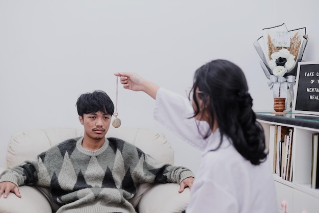 Młody mężczyzna patrzy na wahadło, które trzyma kobieta psychiatra podczas sesji hipnoterapii w biurze