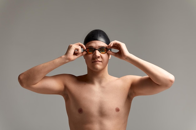 Młody mężczyzna pływak przygotowuje się do startu, szczegół portret pływaka w masce i kapeluszu, szare tło, kopia przestrzeń, koncepcja pływania.