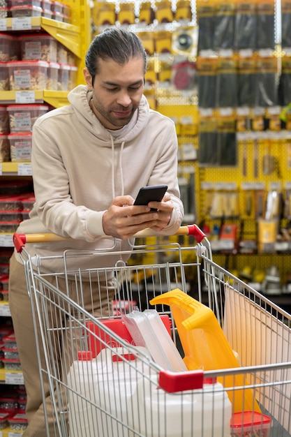 Młody mężczyzna pochylający się nad koszykiem podczas przewijania w smartfonie