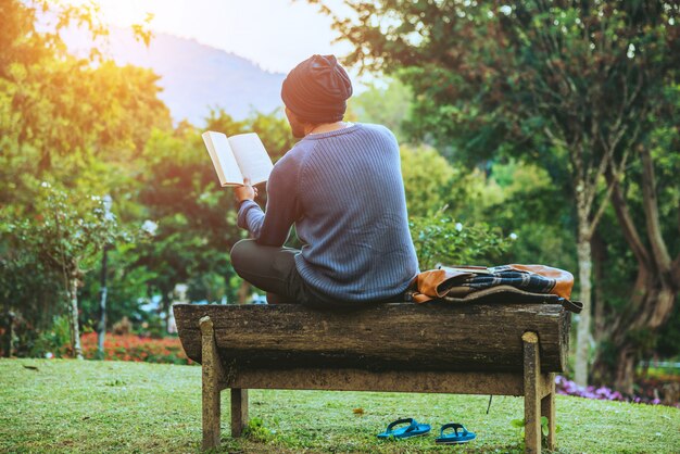 Młody mężczyzna podróżuje po górach, siedzi i odpoczywa, czytając książkę w ogrodzie kwiatowym.